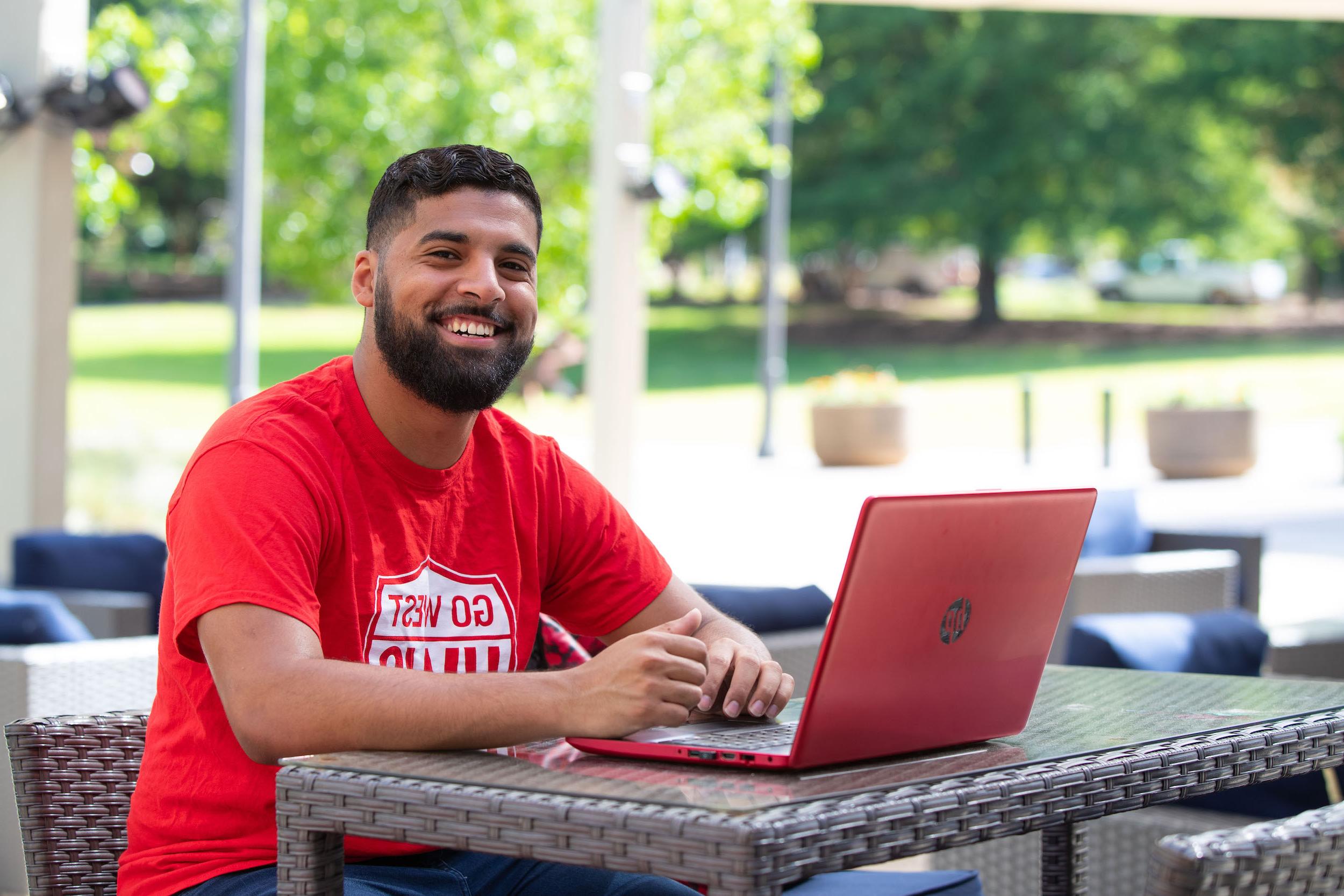 Male student smiling outside with red laptop.